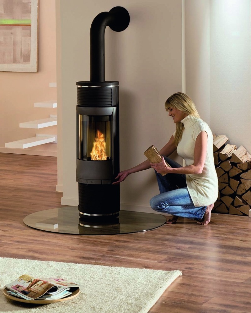 Frau befüllt einen Kaminofen und lächelt dabei zufrieden